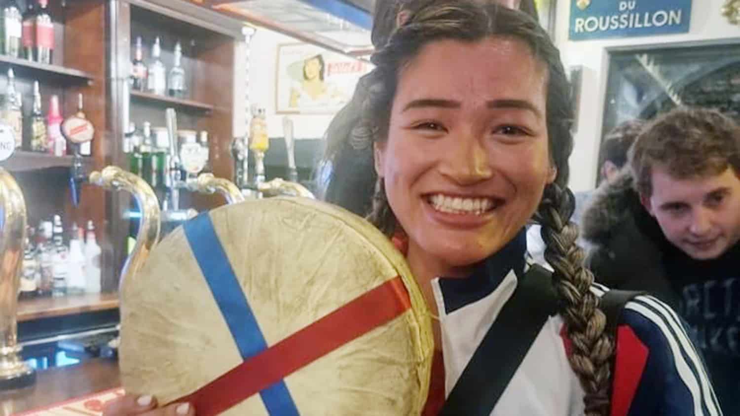 Abby Lampe in an English pub holding up the cheese wheel she won.